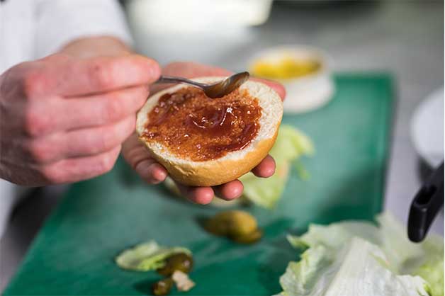 Chef is spreading sauce along the bottom of the lid of the milk bun