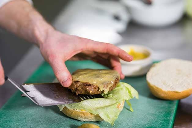 The chef is placing the cooked patty with cheese on the milk bun