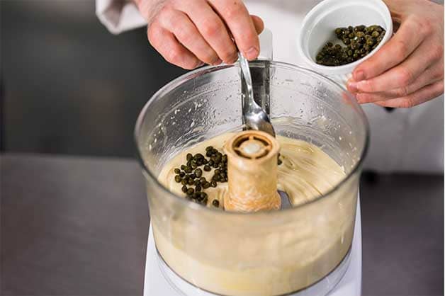Chef dropping in capers into the blender