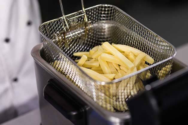 Chef frying chips in deep fryer