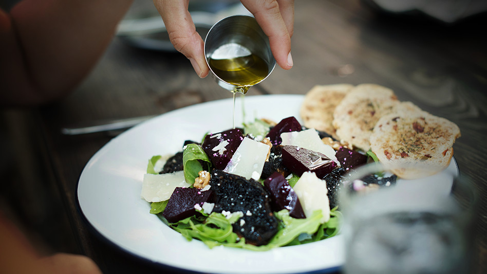 The image shows someone pouring oil over a salad