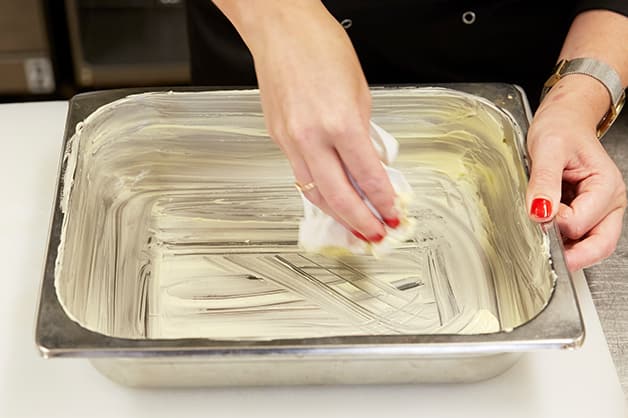 The chef is seen buttering the baking dish