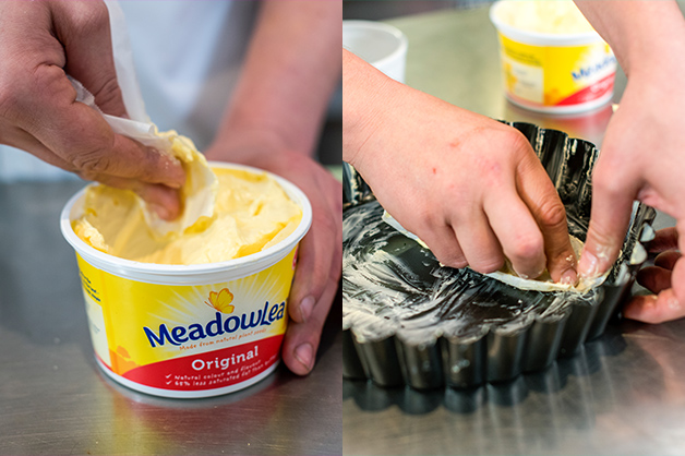 The chef is seen using margarine to coat the pie dish