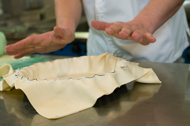 The chef is seen stretching the Pampas Shortcrust Pastry over the dish