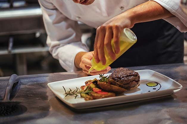 The image shows the chef using oils as a dressing for his meat