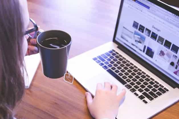 A lady is pictured holding a cup of tea and researching the laptop