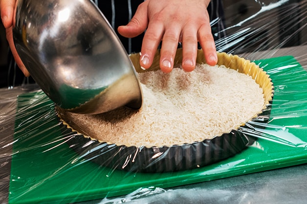 Chef is seen filling the raw shell with rice for blind baking