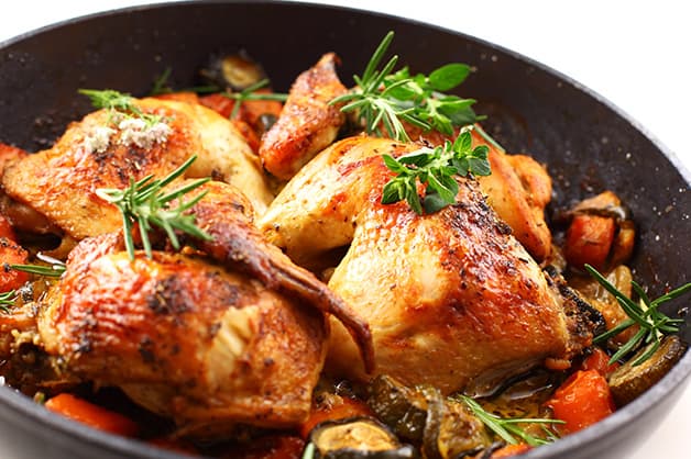 Chicken being fried in a pan with vegetables and oil