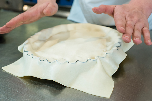 The photo shows the chef cutting around the edges of the lid