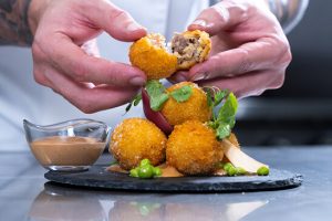 A plate of crispy fried confit duck croquettes with oli & vine aioli being served by a che